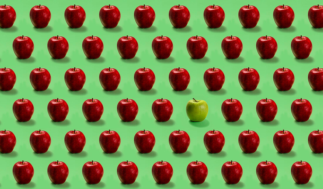 Group of red apples and one green on green background