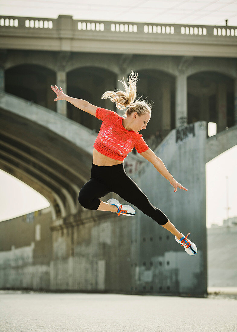 Sportliche Frau beim Springen im urbanen Umfeld
