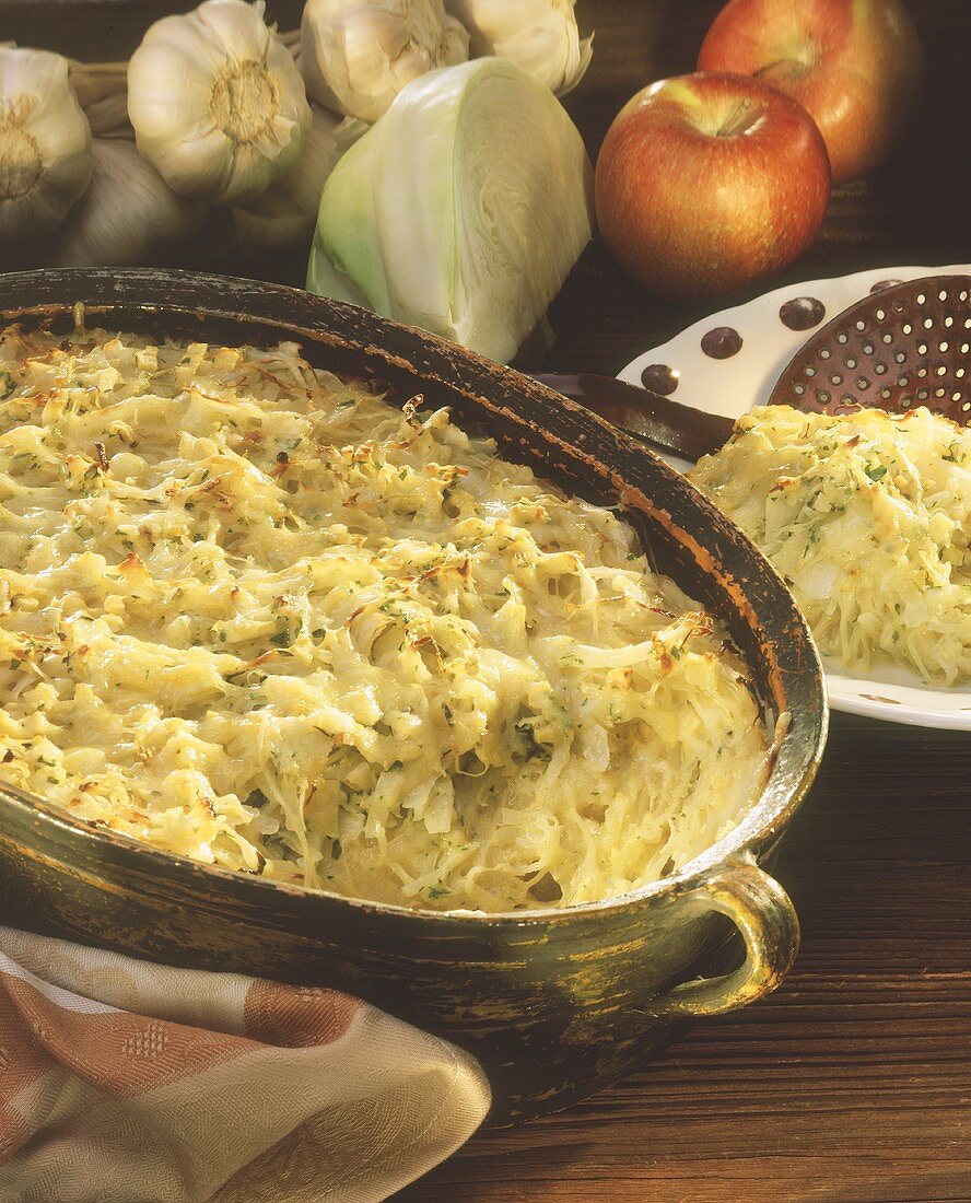 Weisskohlgratin in einer Form, Deko: Kohl, Knoblauch, Äpfel