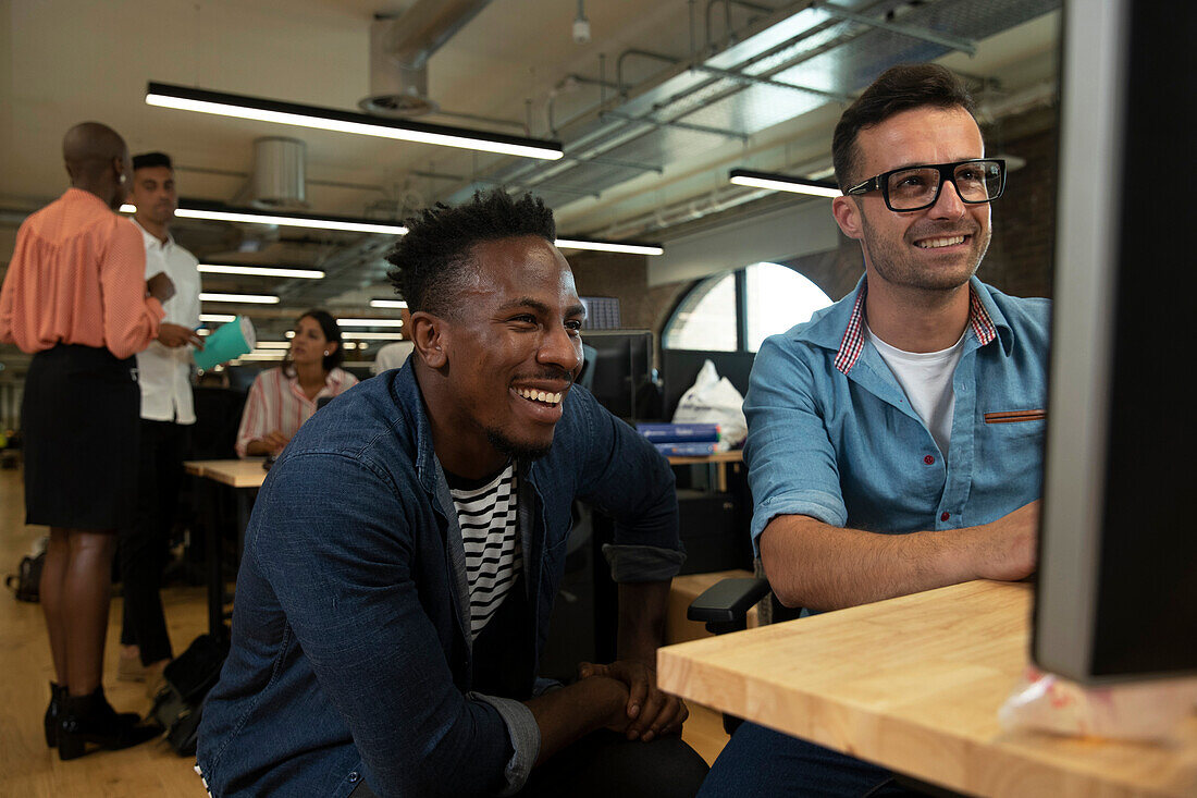 Happy businessmen working at computer in open plan office