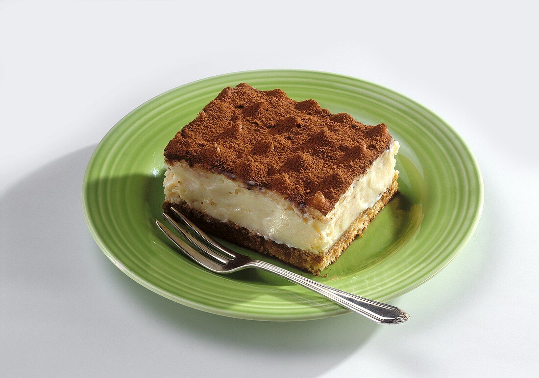 A piece of tiramisu on green plate with fork