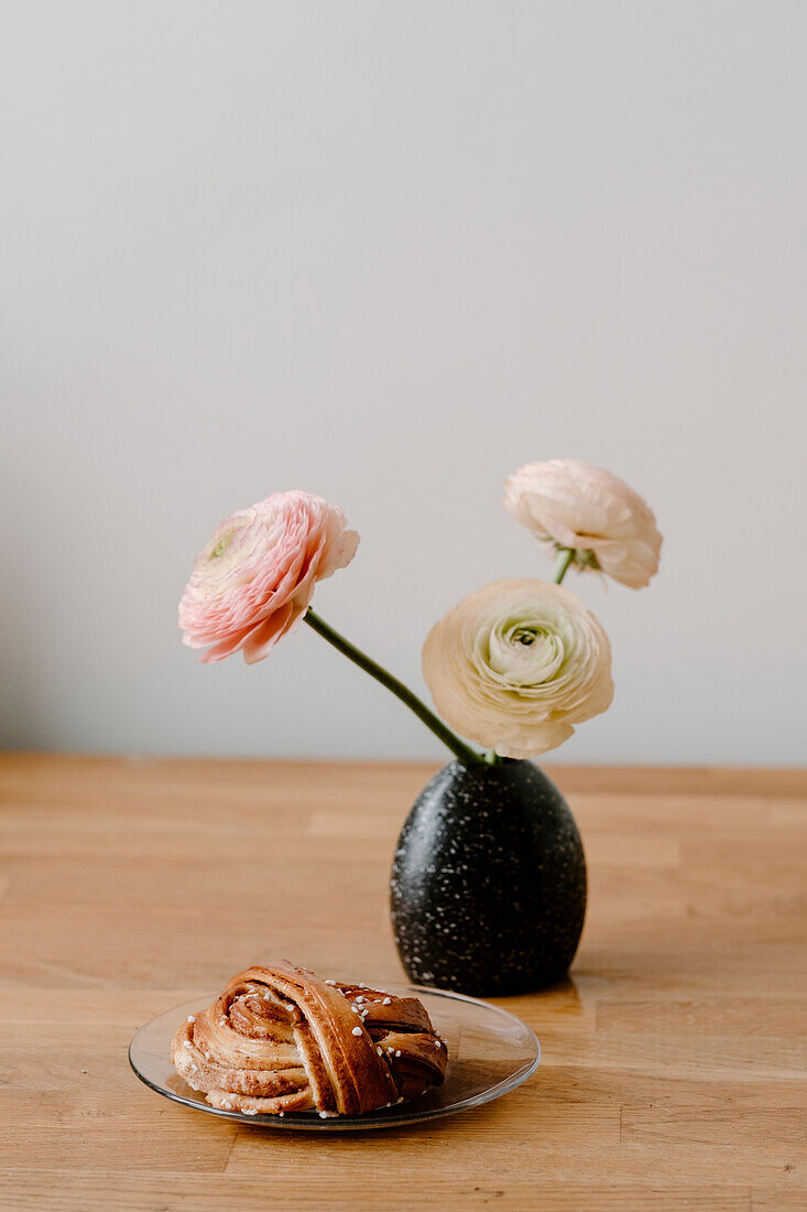 Persian buttercup flowers in vase and cinnamon bun on plate