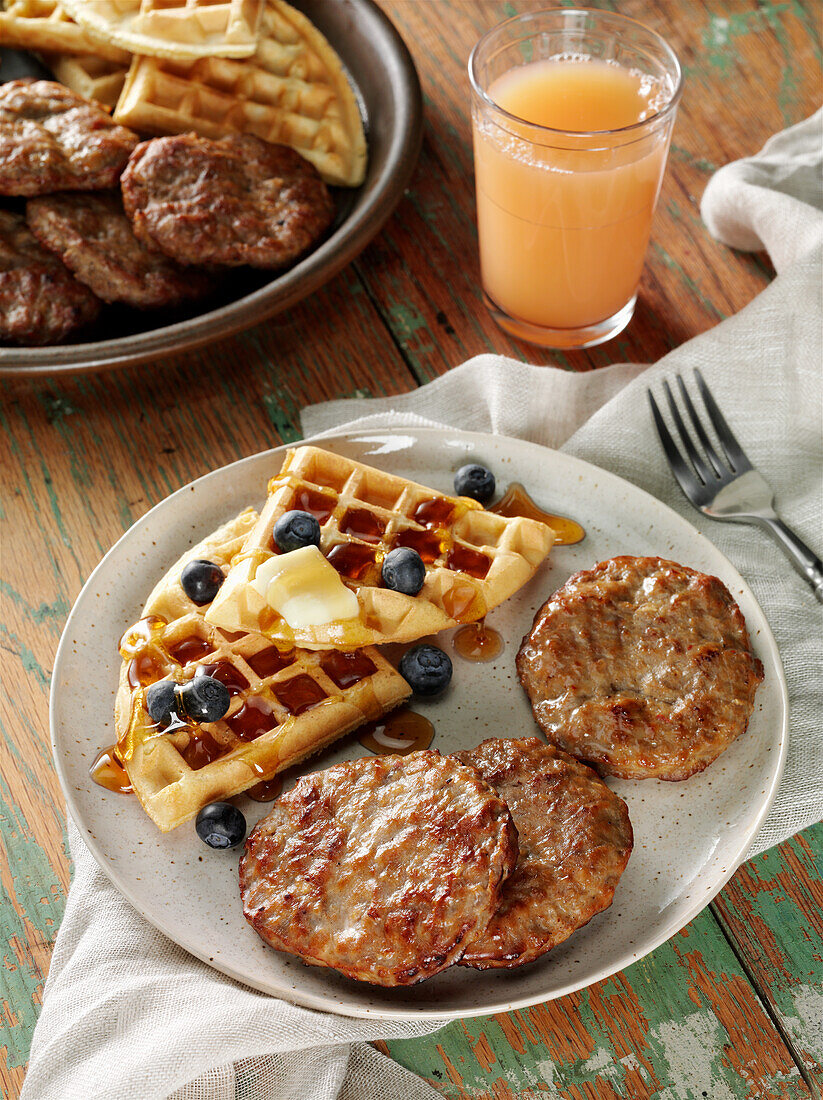 Beef breakfast sausage patties with waffles, blueberries, butter and maple syrup, a glass of grapefruit juice