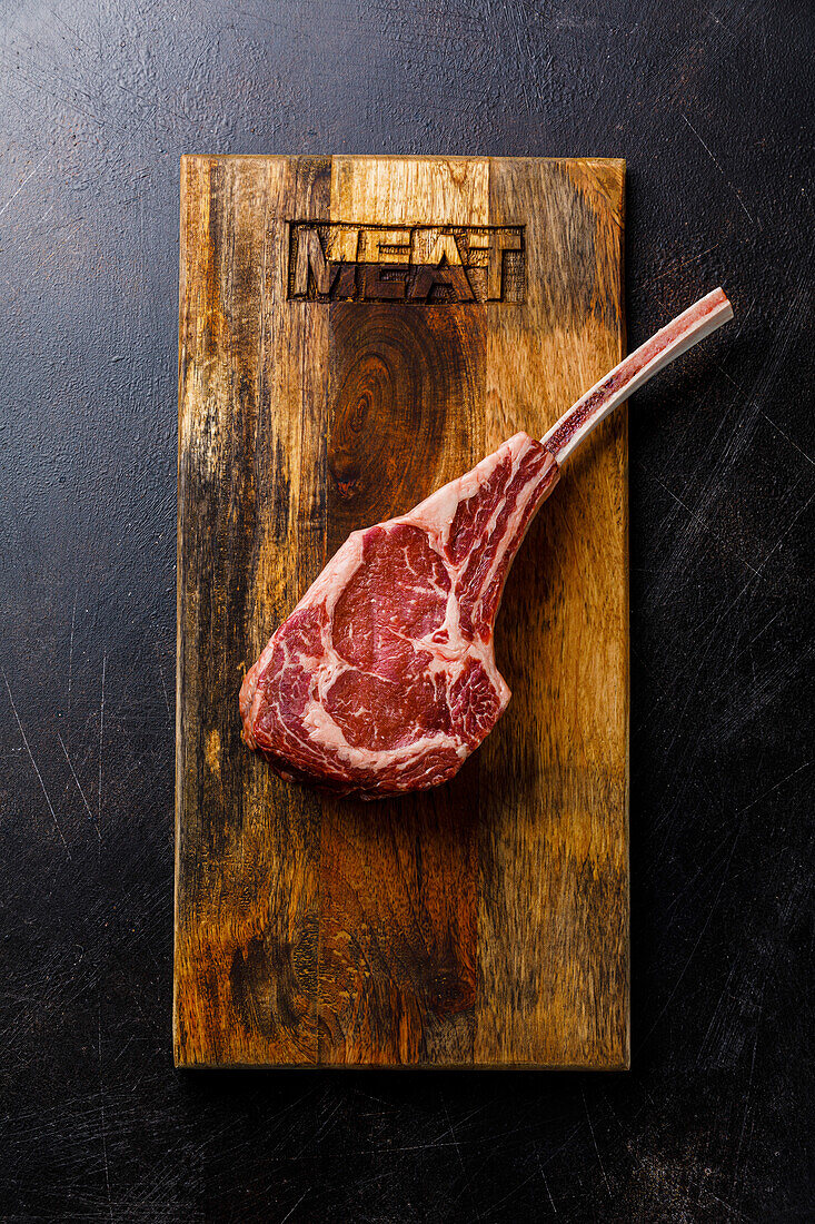 Raw fresh meat Tomahawk Steak on wood board on dark background
