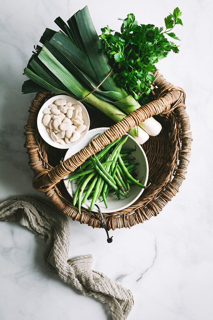 Basket of green vegetables and beans on a marble surface