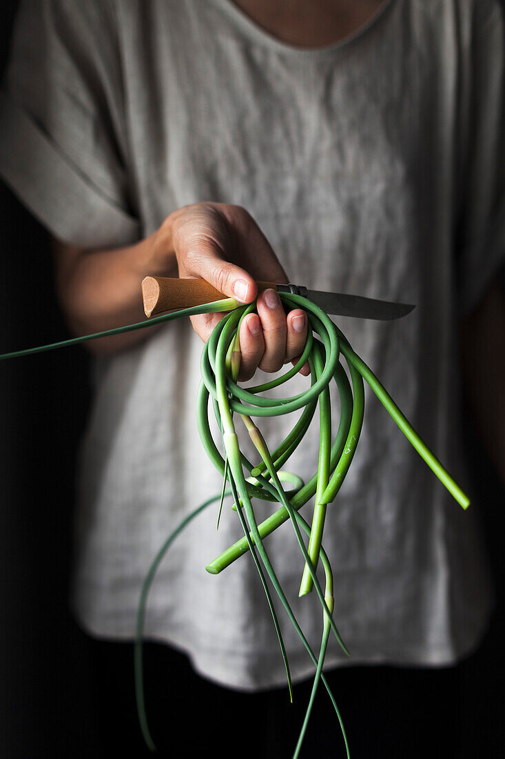 A person holding fresh garlic scapes