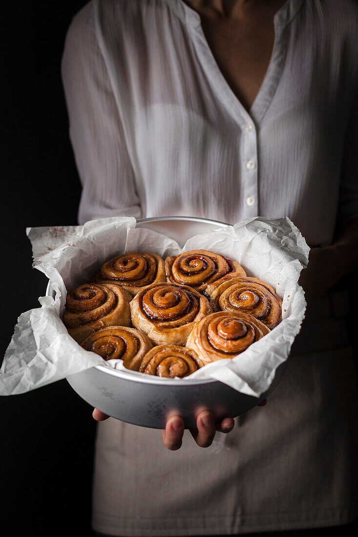 A person holding a baking pan of cinnamon rolls