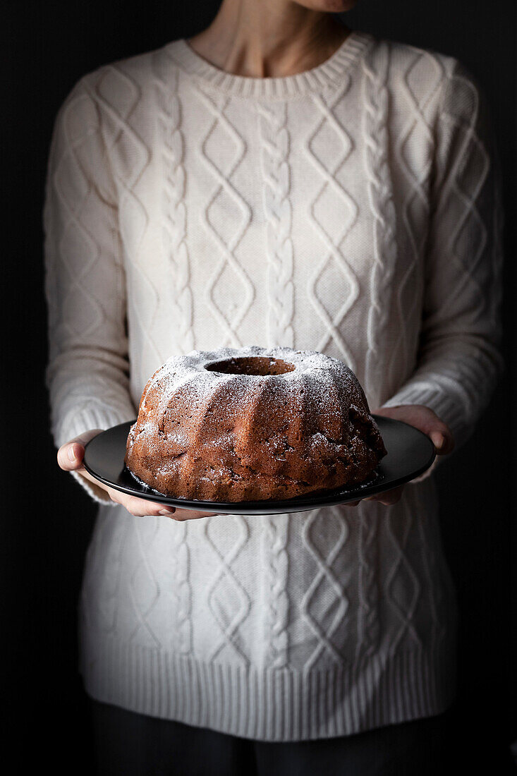A person in a cozy sweater holding a bundt cake.