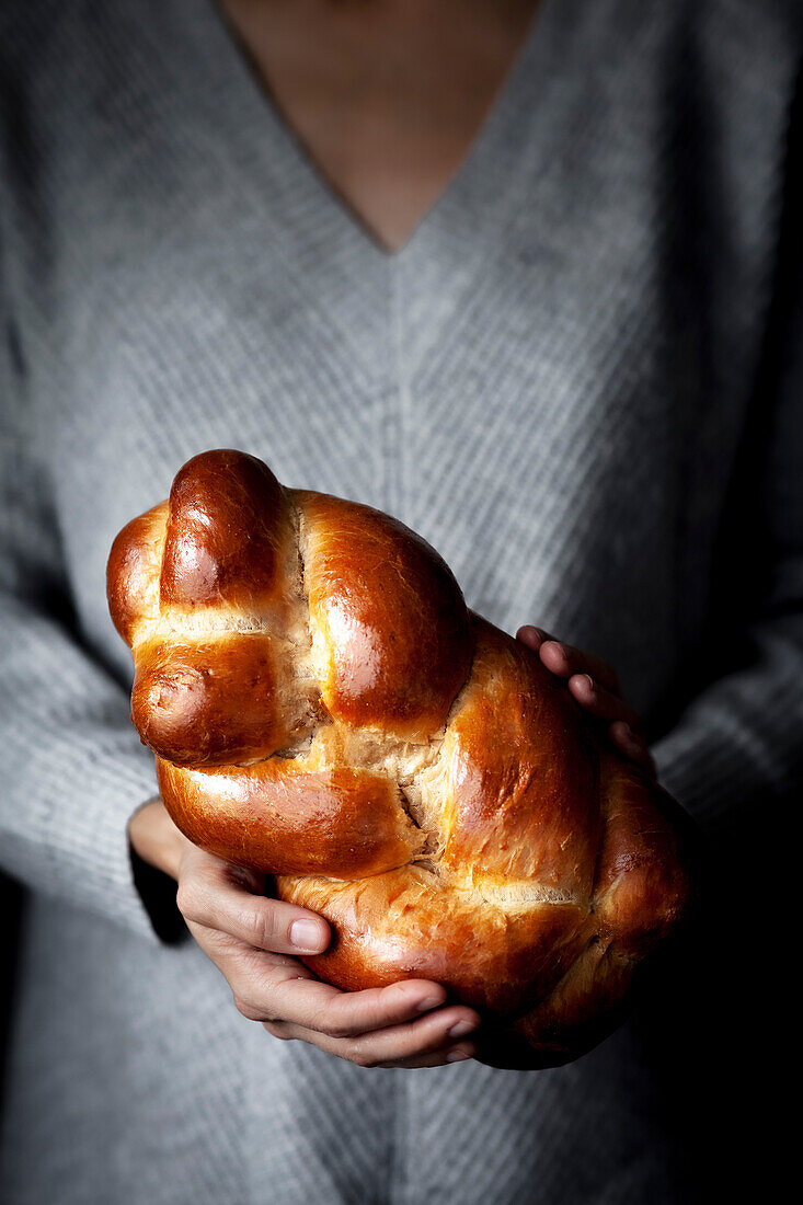 A person holding a loaf of brioche bread.