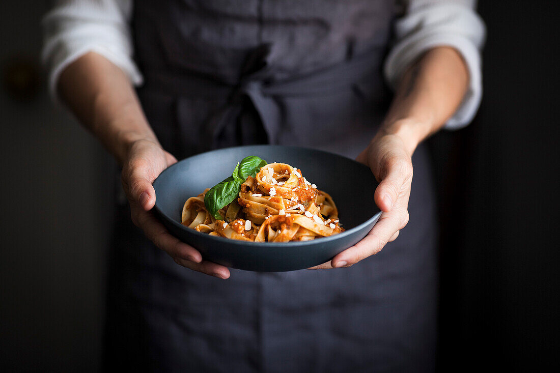 A blue bowl of pasta and tomato sauce held by a cook