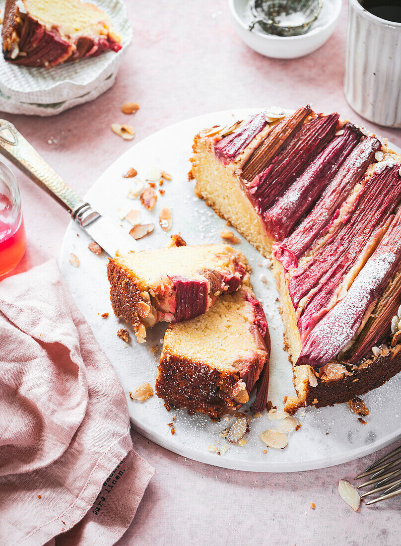 A Rhubarb and Almond Cake on a Marble Board with Cake Slices and Coffee Mug