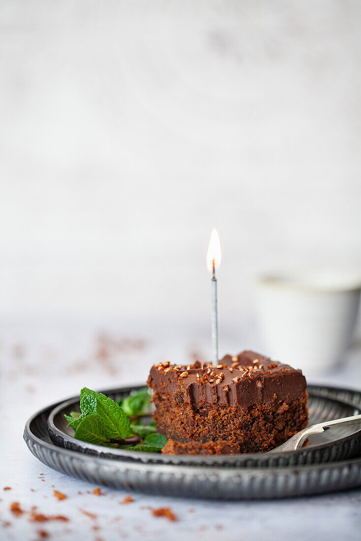 Ein Stück Schokoladenkuchen mit Ganache und brennender Kerze