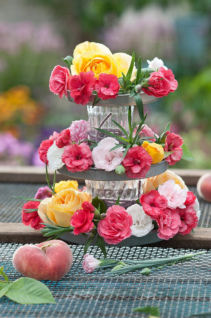 Self-made cupcake stand made of zinc coasters and glasses as fragrant decoration with roses and carnation blossoms
