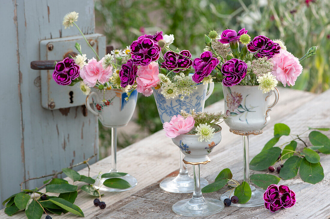 Unusual decoration idea with carnations, Knautia, and Queen Anne's Lace in cups on glass base, branch of Shadbush