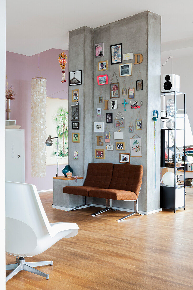 Pictures, photos and decorative letters on concrete partition with brown armchairs below in open-plan interior