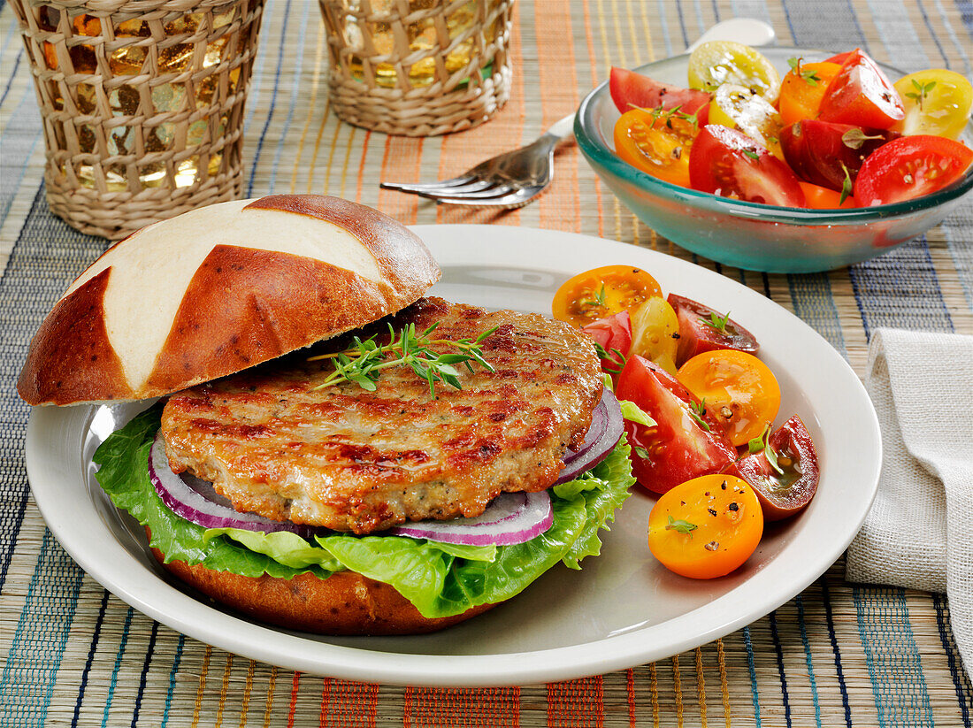 Chicken-Burger auf Laugenbrötchen mit Salat und Zwiebeln dazu Tomatensalat