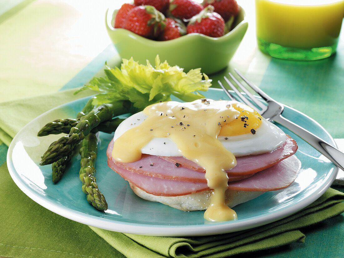 Canadian bacon and a fried egg with hollandaise sauce on an English muffin with asparagus