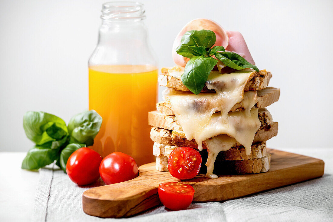Überbackene Sandwiches mit geschmolzenem Käse, Schinken, Kirschtomaten und Orangensaft