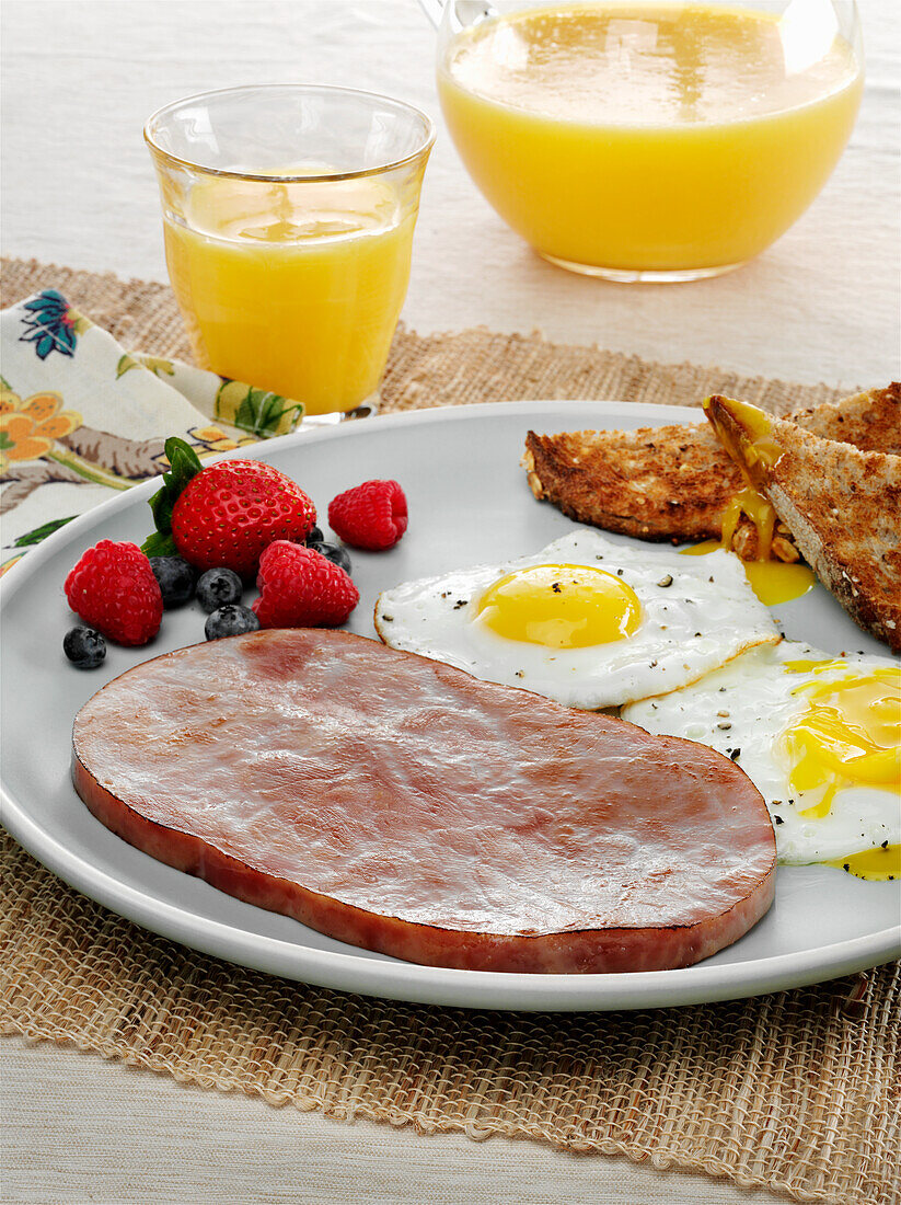 Frühstück mit Schinken-Steak, Spiegelei, Vollkorntoast und Orangensaft