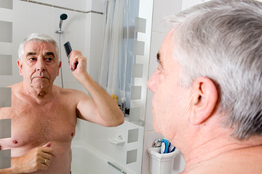 Elderly man combing his hair in front of a bathroom mirror