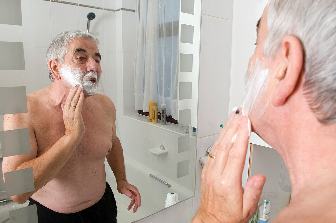 Elderly man shaving in front of a bathroom mirror