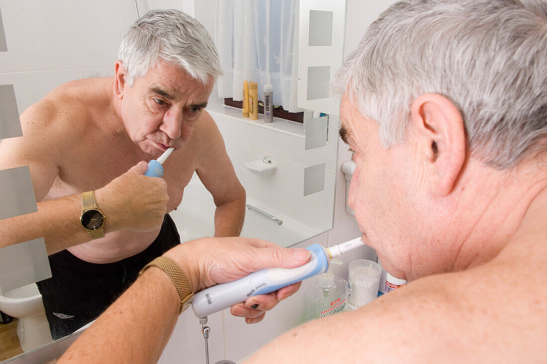 Elderly man using an electric toothbrush to clean his teeth