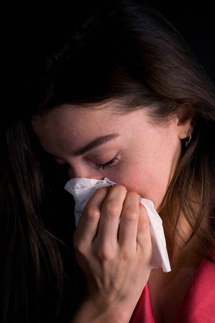 Young woman sneezing into a tissue
