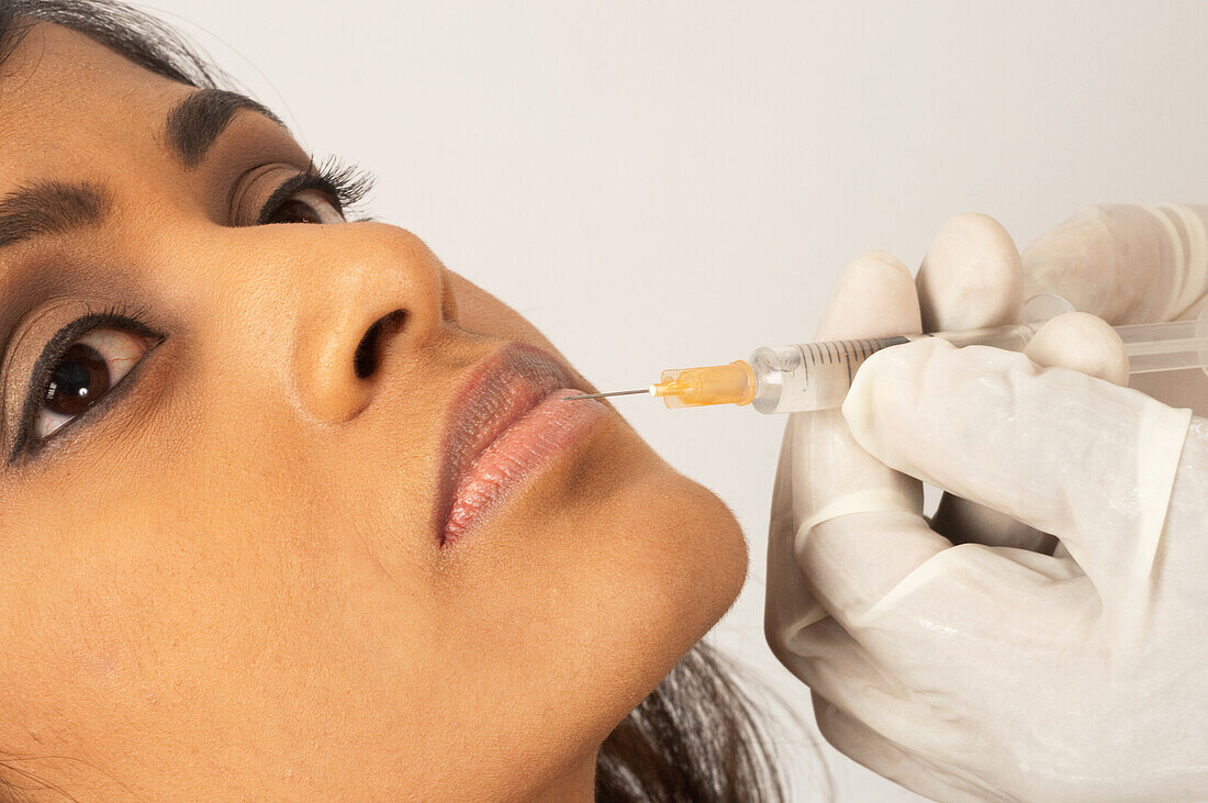 Doctor injecting collagen into a young woman's lip
