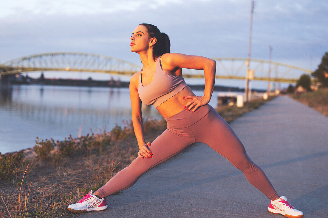 Young jogger woman stretching legs before run at riverside