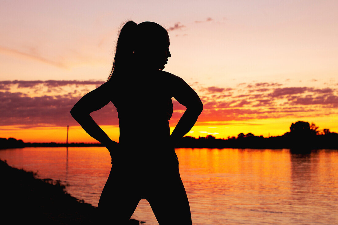 Silhouette of a woman at a riverbank at sunset
