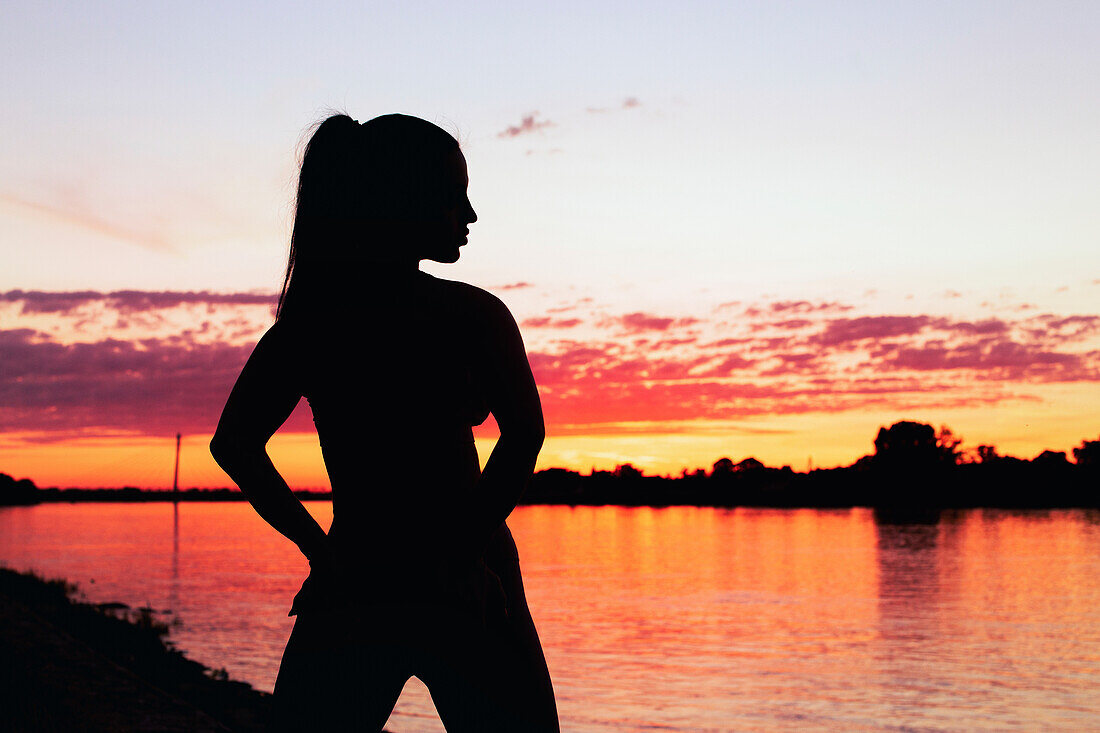 Silhouette of a woman at a riverbank at sunrise