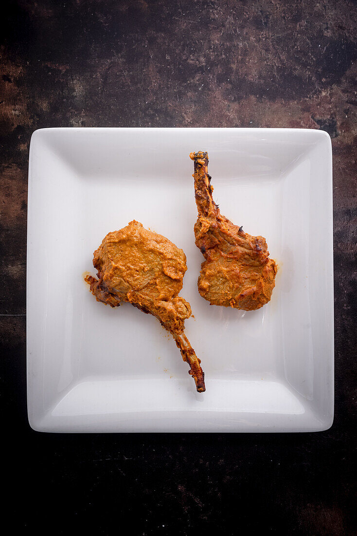 Lamb chops on a plate against a dark background