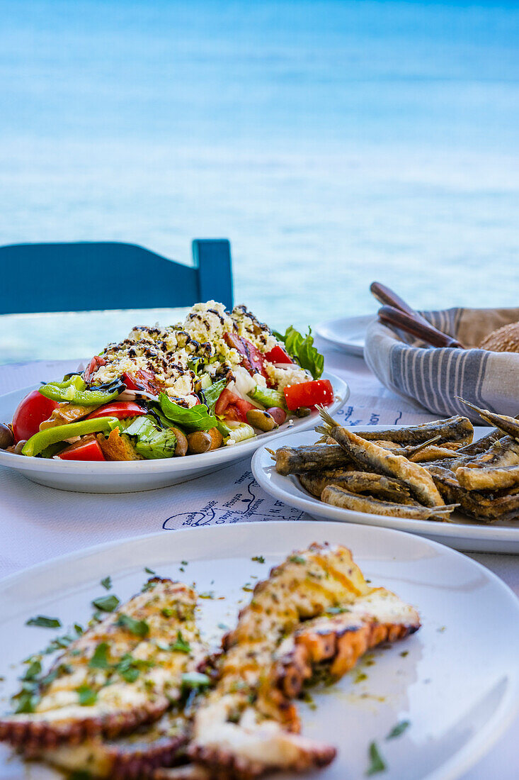 Gedeckter Tisch mit griechischem Salat, Tintenfisch und frittierten Sardinen am Meer