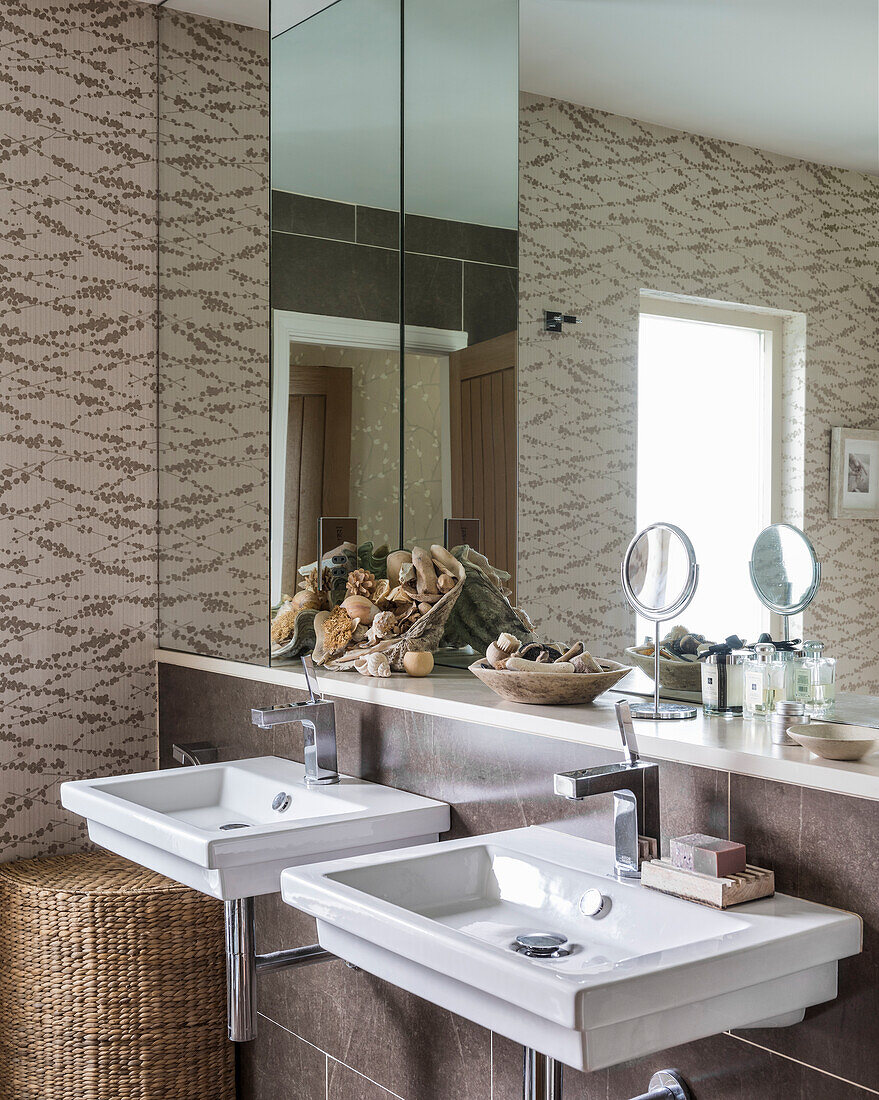 Two washbasins, a shelf and mirrors in a bathroom with patterned wallpaper