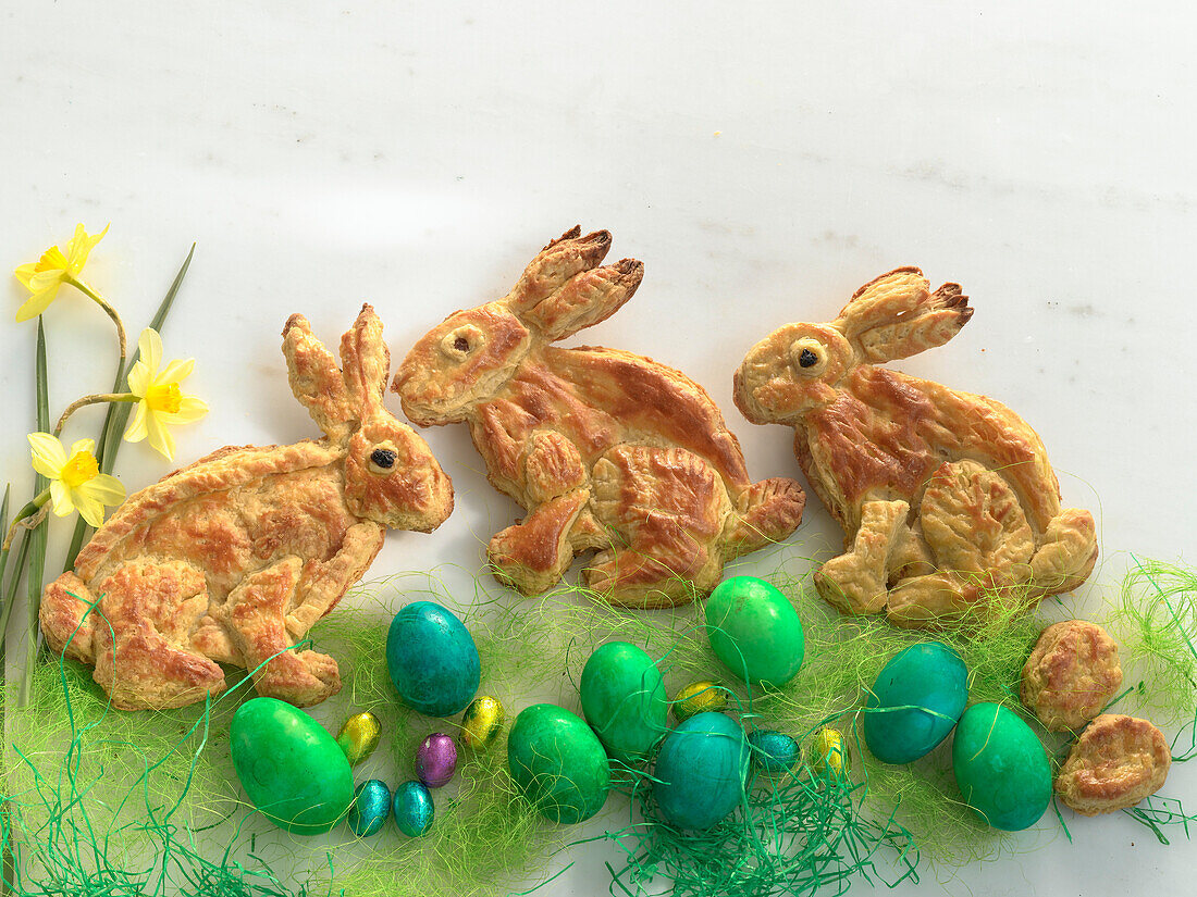 Easter bunnies made of puff pastry decorated with coloured Easter eggs, chocolate eggs, daffodils
