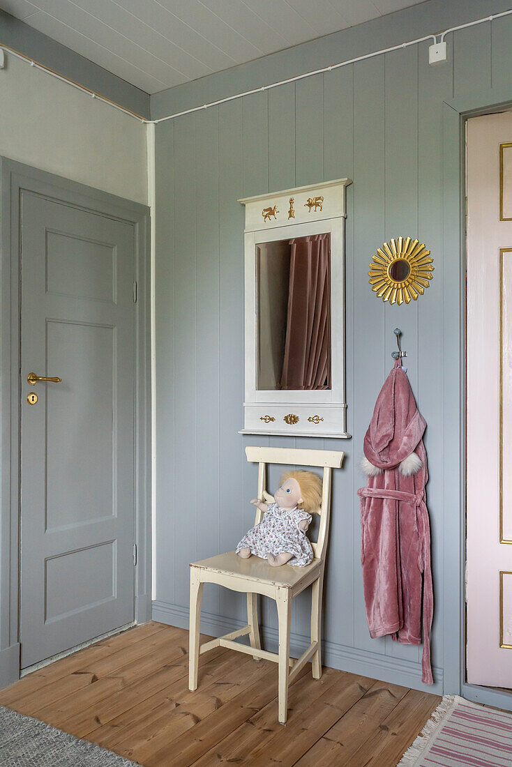 Old wooden chair below mirror in child's bedroom with wood panelling painted light grey