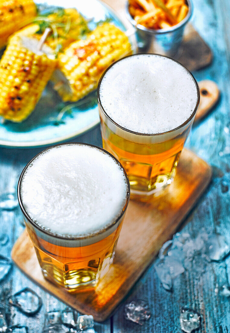Glasses of beer on a blue wooden table sweetcorn corn on the cob and chips