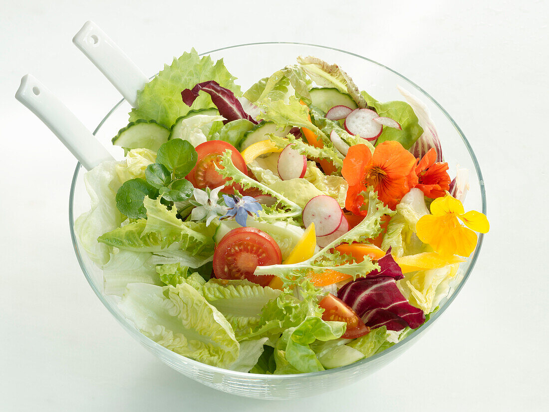 Mixed colourful salad in a glass bowl with salad servers