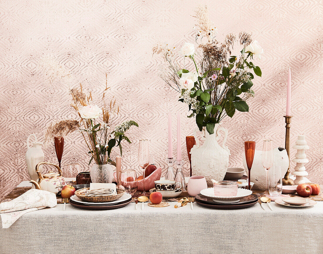 Set table in shades of pink and peach, bouquets of flowers and candles