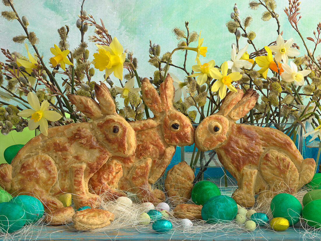 Easter bunnies made of puff pastry, coloured Easter eggs, chocolate eggs, daffodils and willow catkins