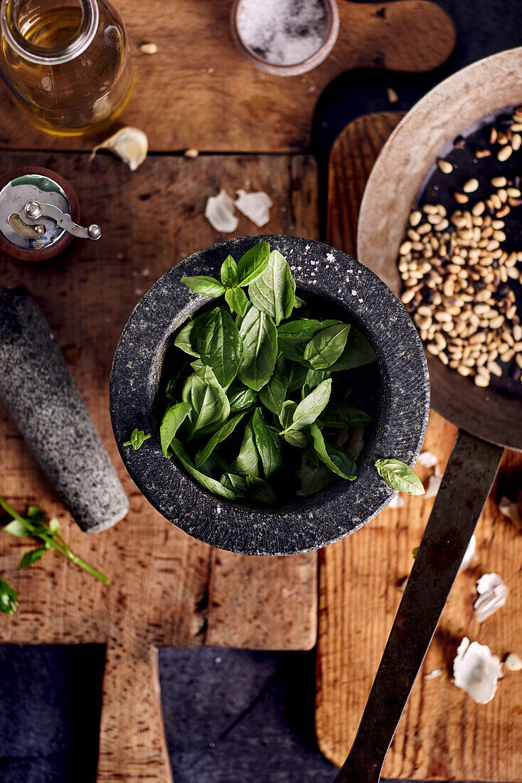 Basil in a mortar next to other ingredients to make pesto