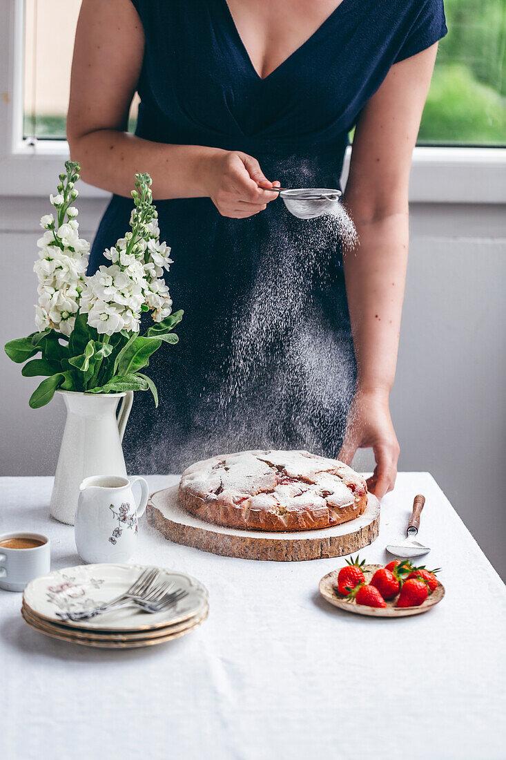 Woman dusting strawberry cake with powdered sugar