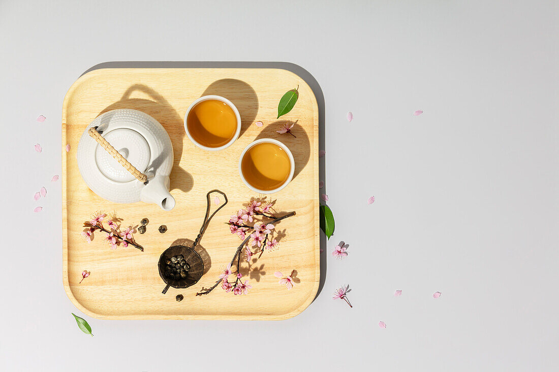 Teekanne, Teebecher, Kirschblütenzweige und Teesieb auf Tablett