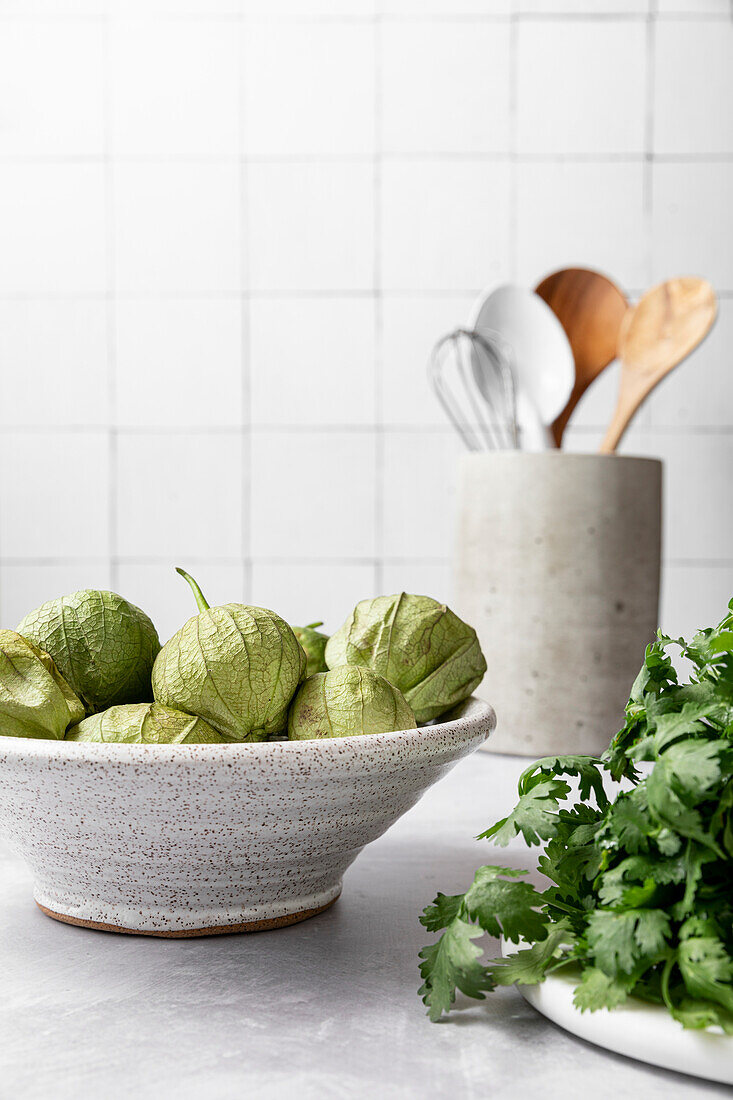 Tomatillos in Keramikschale daneben Koriander und Küchenutensilien