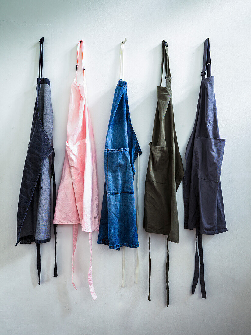 Pink, blue, grey and black cookery aprons hanging in a kitchen