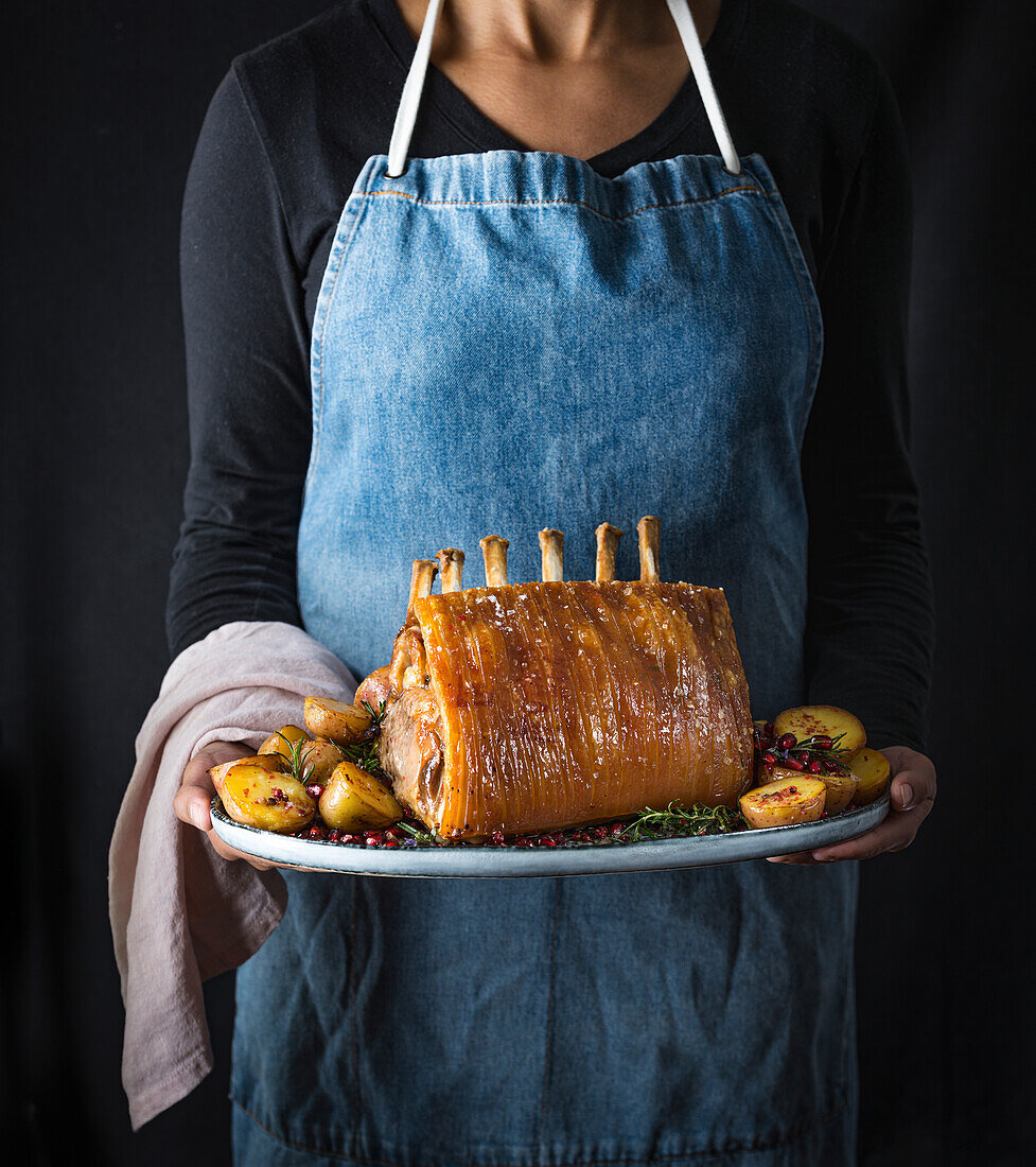 Roast Rack of Pork being held by a chef in a blue denim apron, holding a pink linen towel