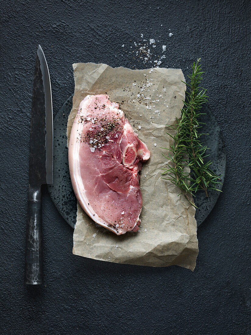 Rohes Schweinekotelett auf Backpapier mit Messer und Gewürzen