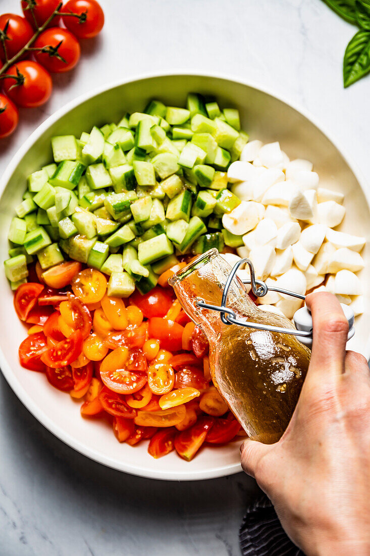 Salat mit Gurken, Tomaten und Mozzarella wird mit Dressing angemacht