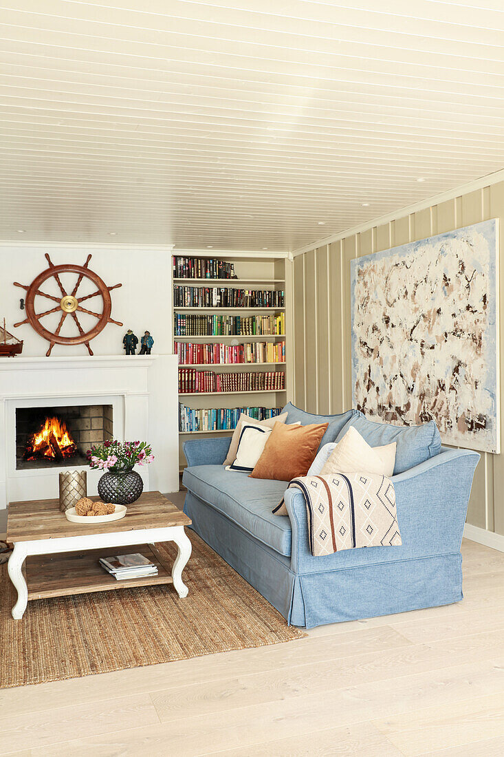 Blue sofa in front of fire in fireplace below ship's wheel on wall