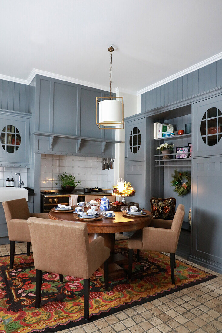 Fitted kitchen with grey cupboards and dining area with round wooden table and upholstered chairs